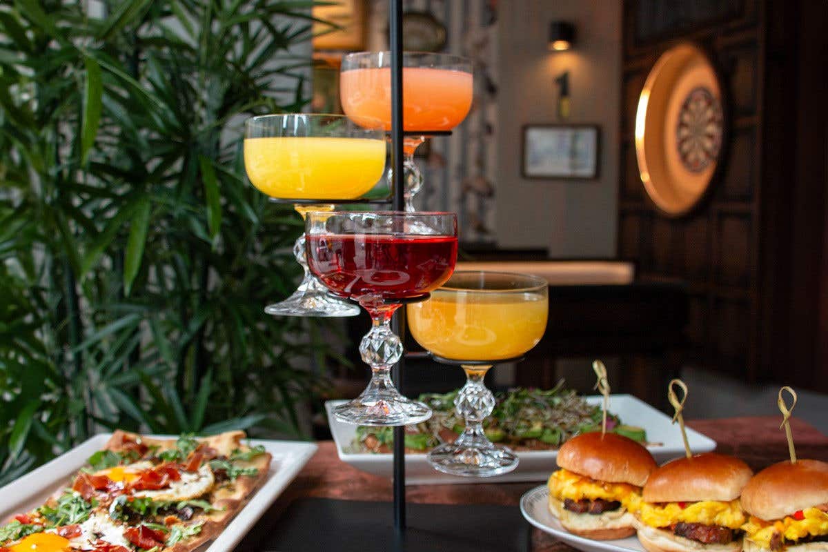 Cocktails hanging on a display case with burgers and pizza on the table behind them
